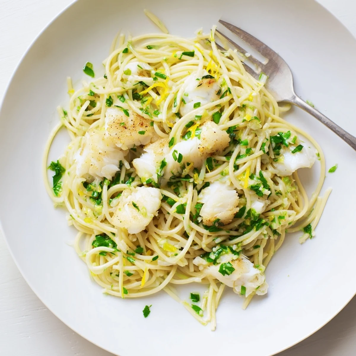 Golden-brown fish flakes nestled among al dente spaghetti, garnished with fresh herbs and lemon wedges for a bright Mediterranean meal.