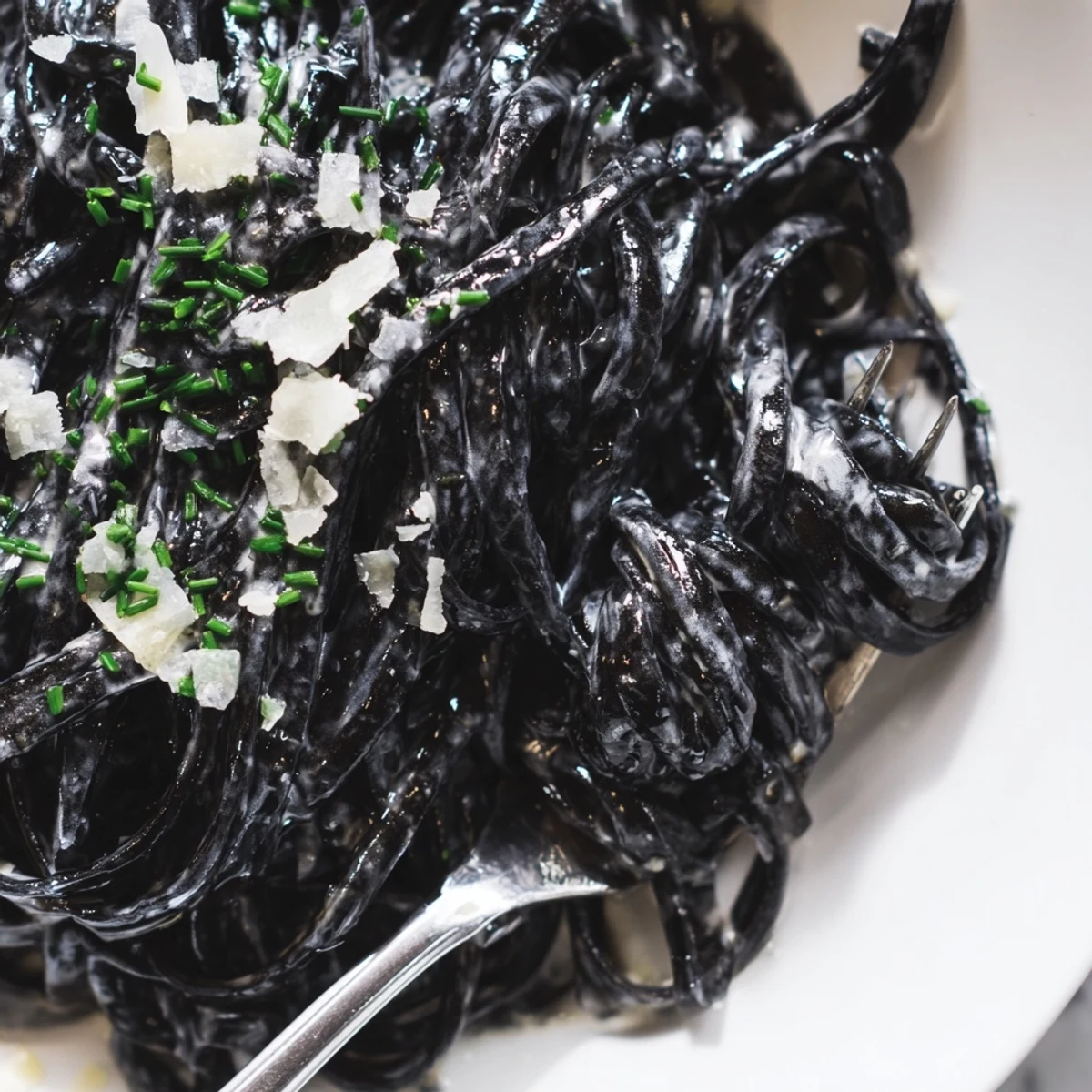 Garnished with fresh parsley and lemon wedges, this dramatic black seafood pasta glistens under soft kitchen lighting.