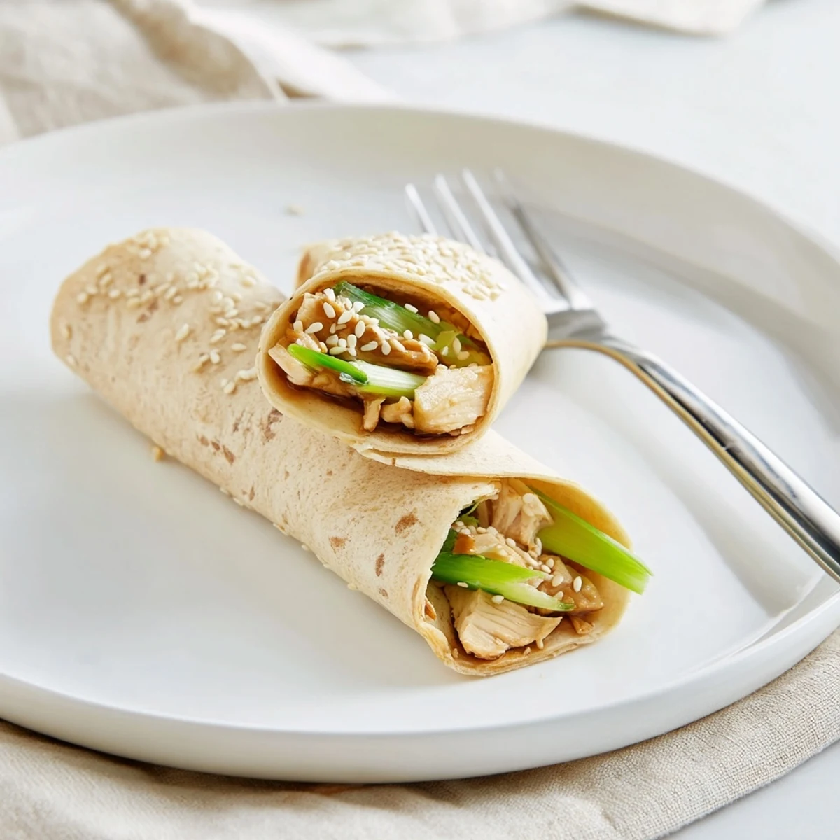 The interior of a freshly cut Teriyaki Chicken Wrap reveals layers of savory chicken, shredded carrots, and fresh spring onions on a clean surface.