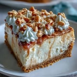 This decadent peanut butter cheesecake is garnished with whipped cream and chopped peanuts on a rustic plate.