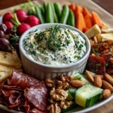 Fresh vegetables, savory meats, and creamy herb dip arranged artfully on a spring-inspired charcuterie board.  