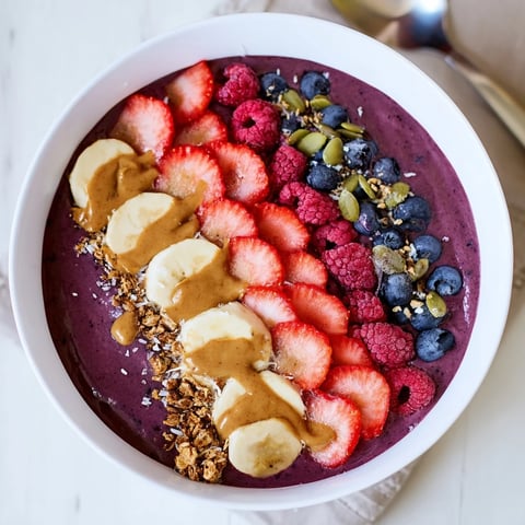 Creamy, vibrant acai berry smoothie bowl topped with fresh sliced banana, mixed berries, and crunchy granola for a nutritious breakfast.