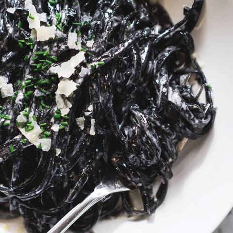 Garnished with fresh parsley and lemon wedges, this dramatic black seafood pasta glistens under soft kitchen lighting.