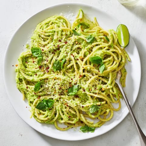 Vibrant green avocado pasta with chili flakes, served warm on a rustic wooden table.  
