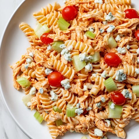 A vibrant bowl of buffalo chicken pasta salad with cherry tomatoes, red bell pepper, and fresh herbs.  
