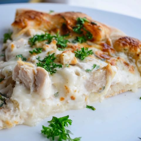 Sliced wedge of Chicken Alfredo Pizza on a wooden board, with creamy sauce and Parmesan visible on each piece.