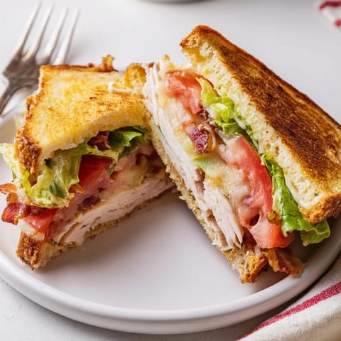 Toasted turkey club grilled cheese with bacon, lettuce, and tomato on golden sourdough slices.