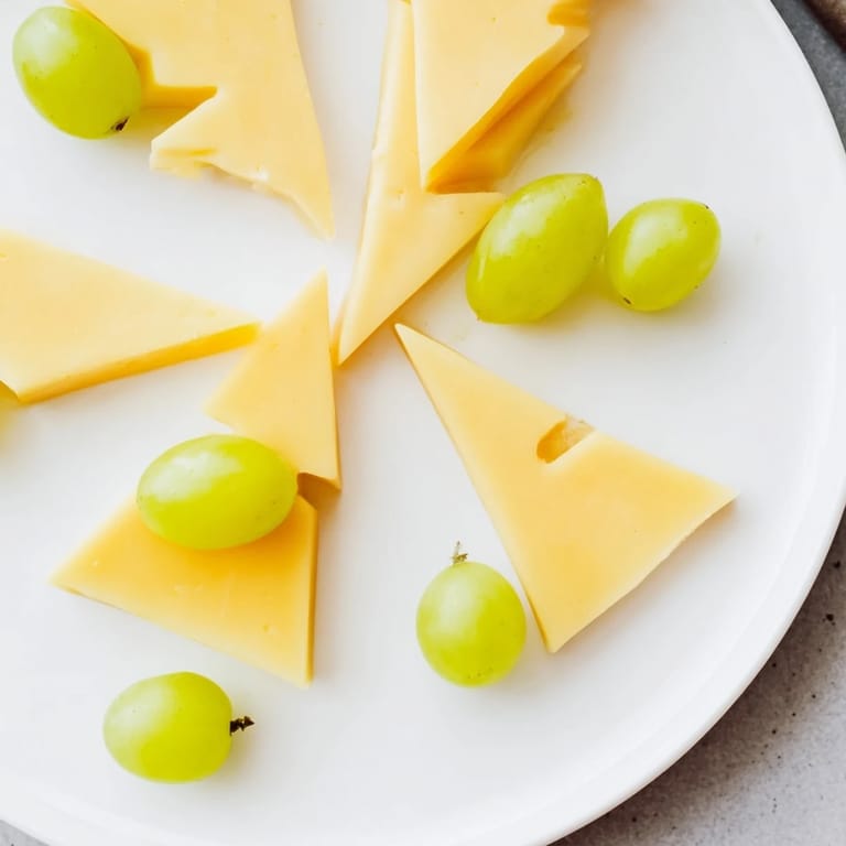 A close-up of The Tannenbaum Border cheese board, showcasing artful cheese triangles with vibrant green grapes.