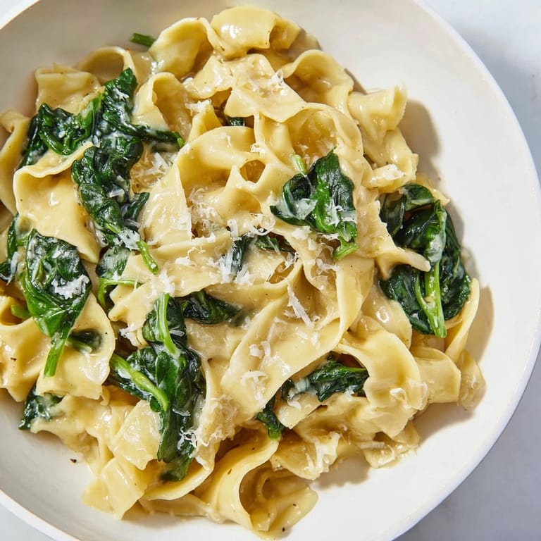 Overhead view of Creamy Spinach Garlic Noodles garnished with extra Parmesan and red pepper flakes beside a glass of white wine.