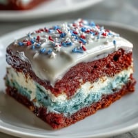 Festive Patriotic Poke Cake generously topped with creamy white chocolate ganache.